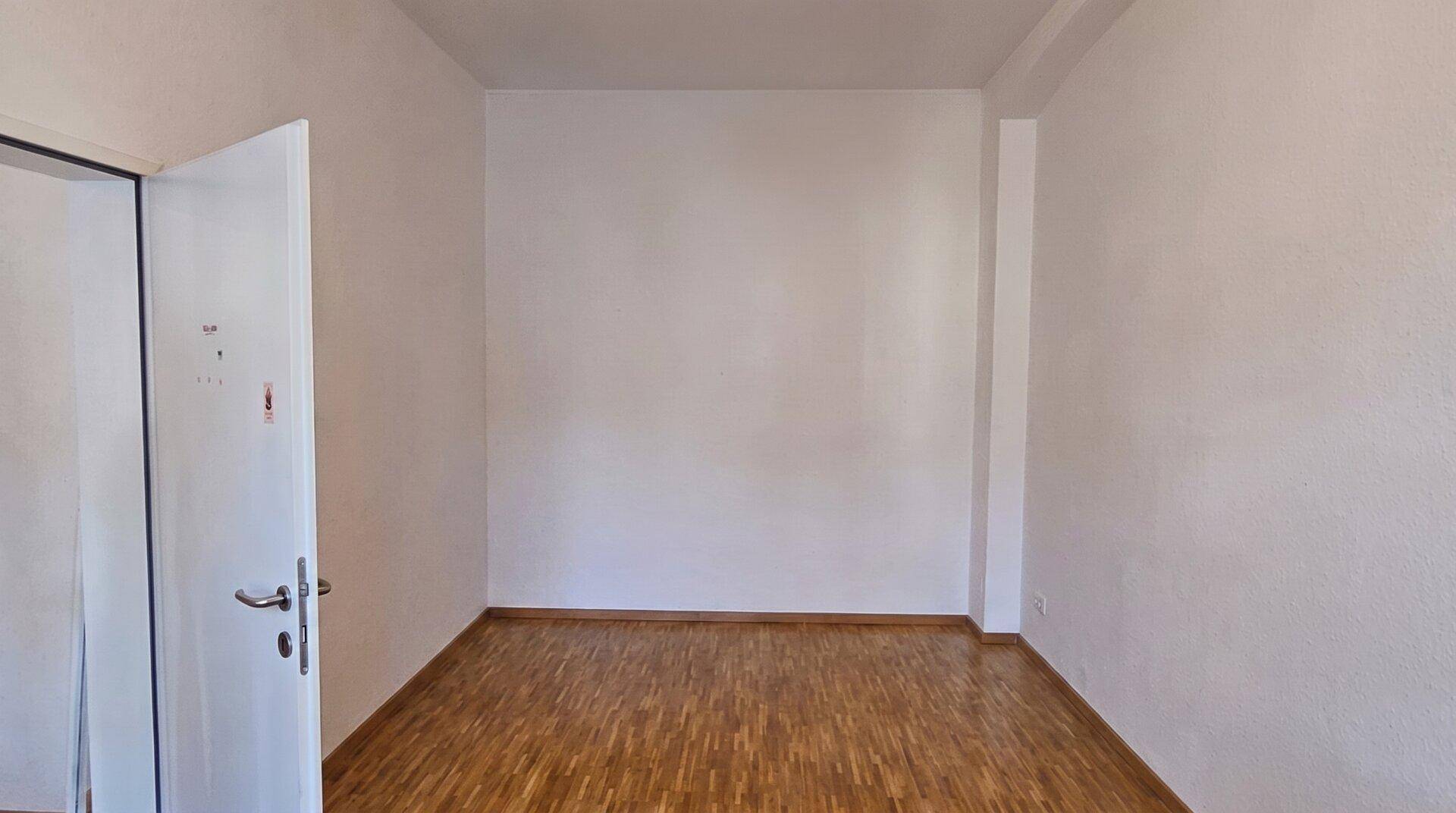 Leerer Raum mit hellen Wänden und warmem Holzfußboden, bereit für individuelle Gestaltung und Nutzung.