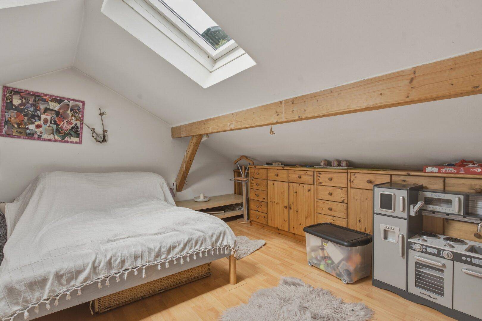 Dachzimmer mit Bett, Holzmöbeln, Dachschräge und Dachfenster für natürliches Licht.