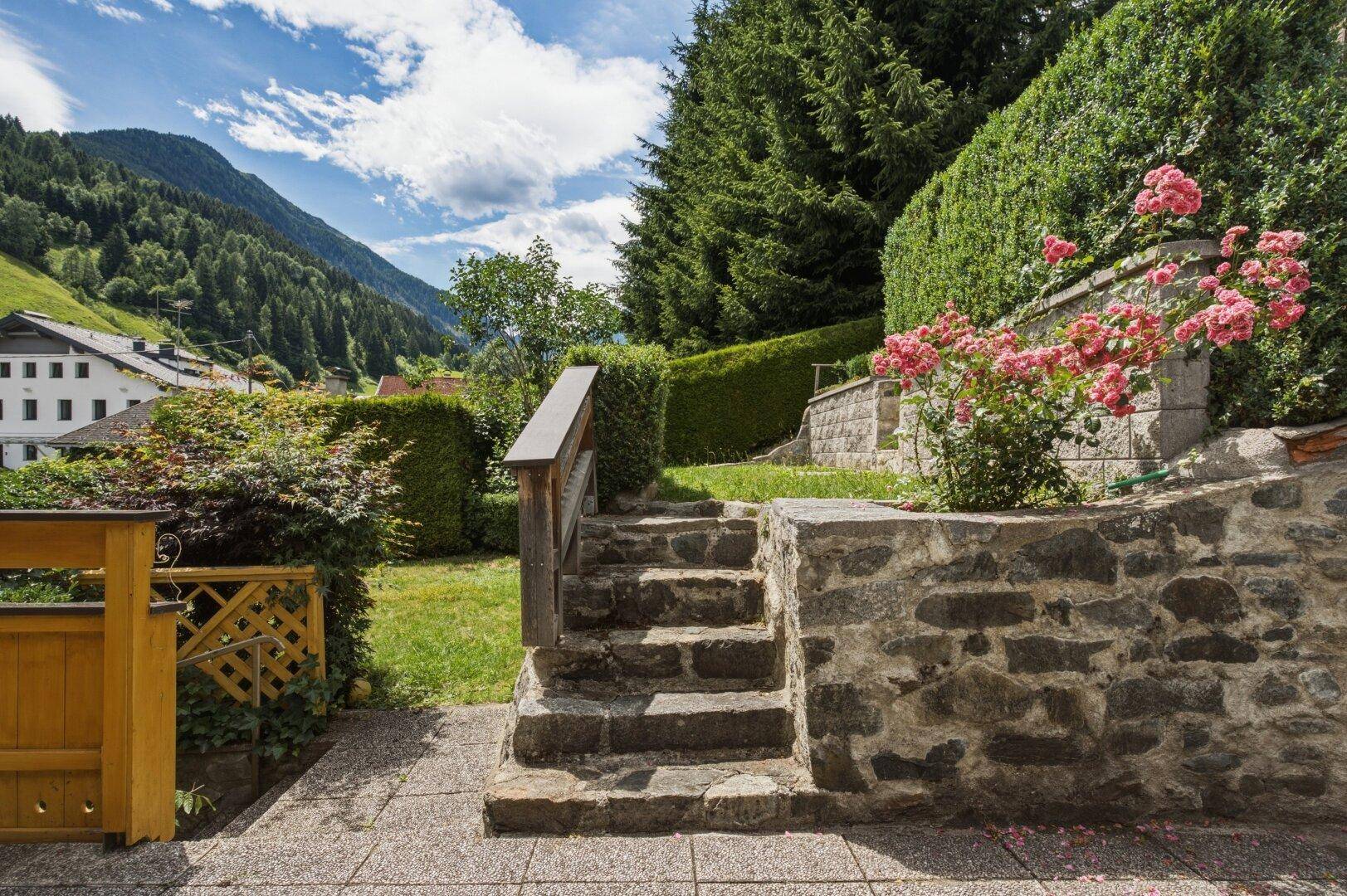 Terrassierter Garten mit Steinmauern, Rosenbeeten und Blick auf die umliegenden Berge.