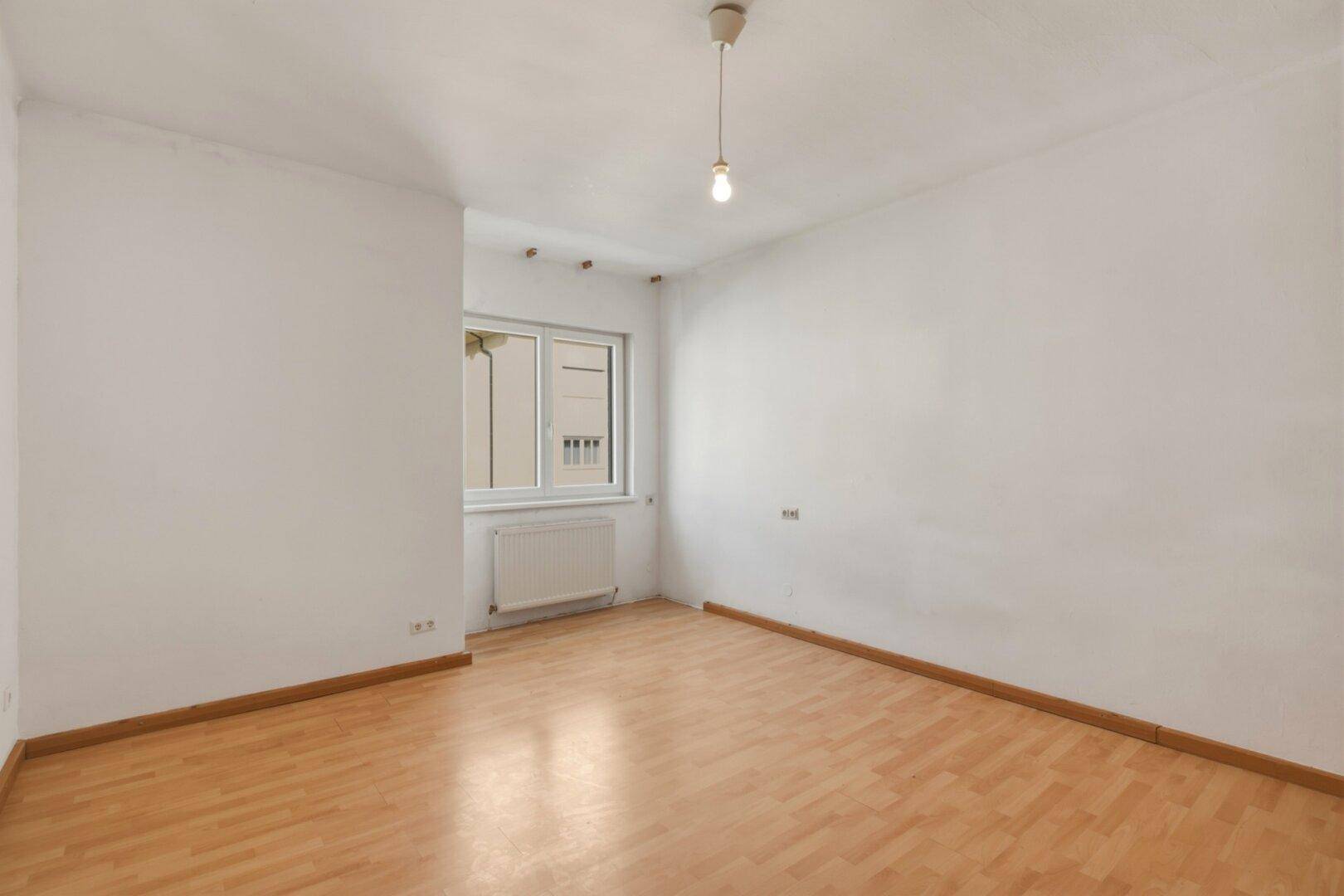 Helles, leeres Schlafzimmer mit Laminatboden und einem Fenster, bereit zur individuellen Gestaltung.