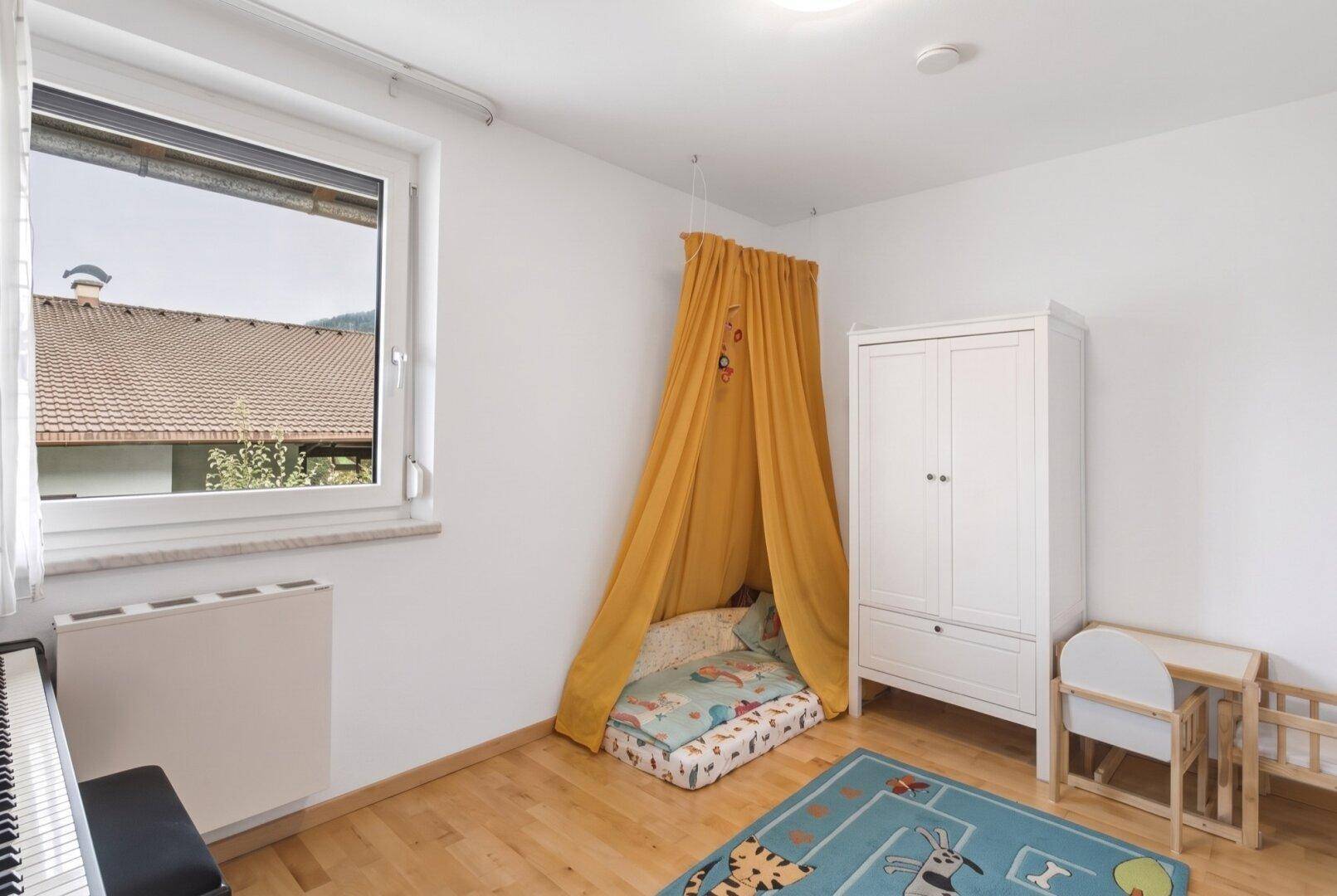 Helles Kinderzimmer mit gelbem Betthimmel, weißem Kleiderschrank und Holzboden.