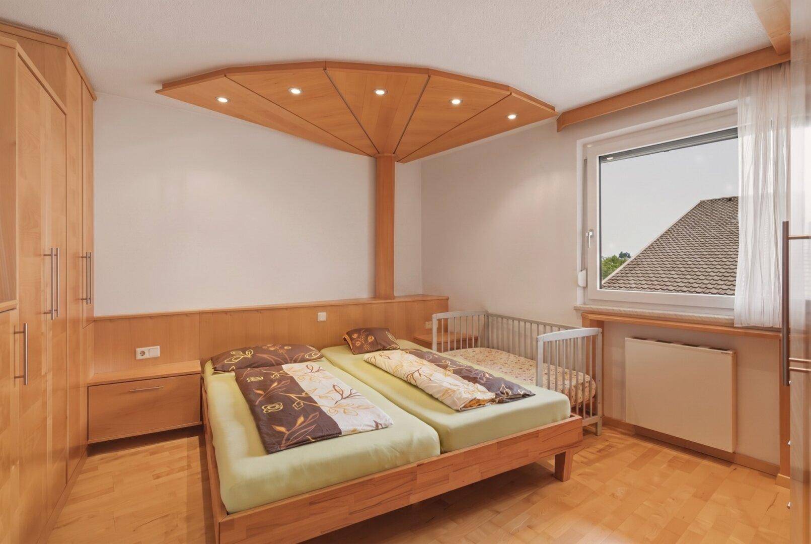 Schlafzimmer mit zwei Einzelbetten, Babybett und maßgefertigten Holzmöbeln unter einem Fenster.