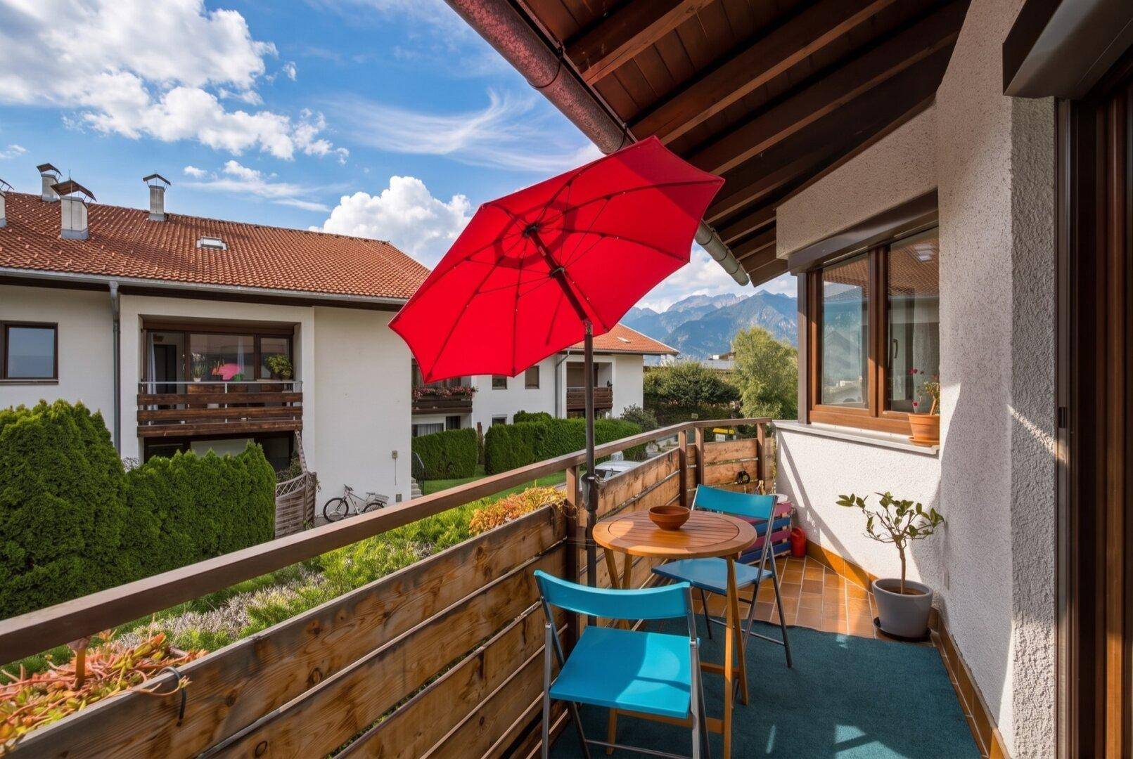 Gemütlicher Balkon mit Sitzgelegenheiten, rotem Sonnenschirm und malerischem Bergblick.