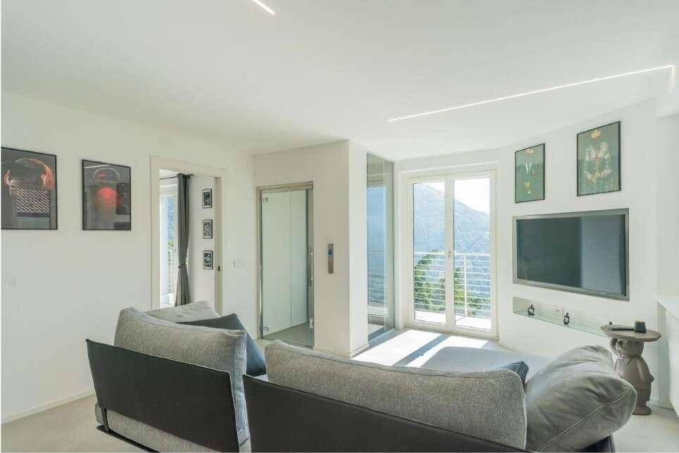 Helles Wohnzimmer mit Zugang zum Balkon, einem gläsernen Aufzug und weitem Blick auf die Berge.