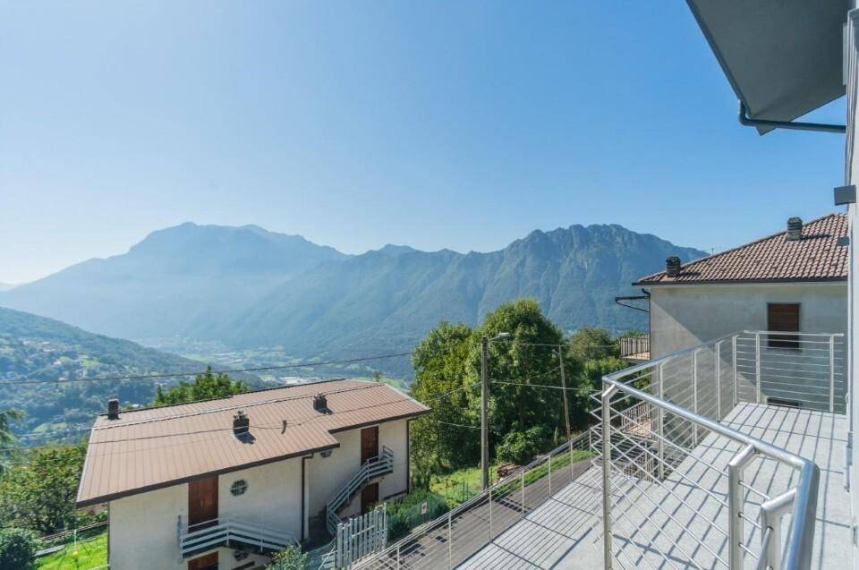Blick von einem Balkon oder einer Terrasse auf die weite Berglandschaft und umliegende Häuser.