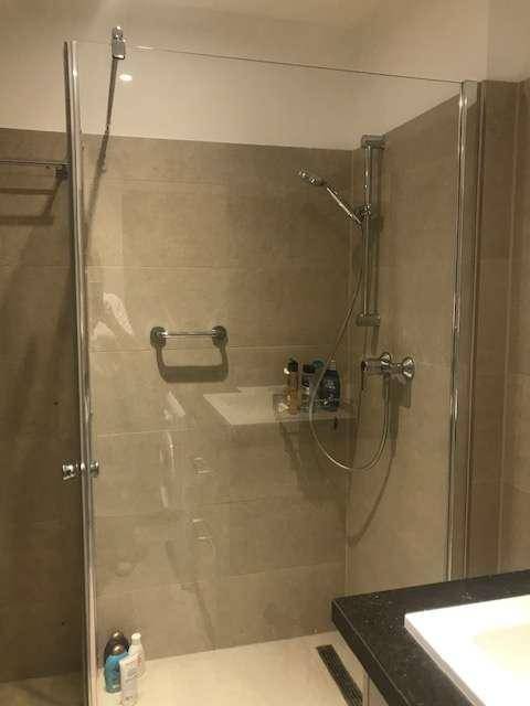 Modernes Badezimmer mit begehbarer Dusche, Glasabtrennung und beigefarbenen Fliesen.