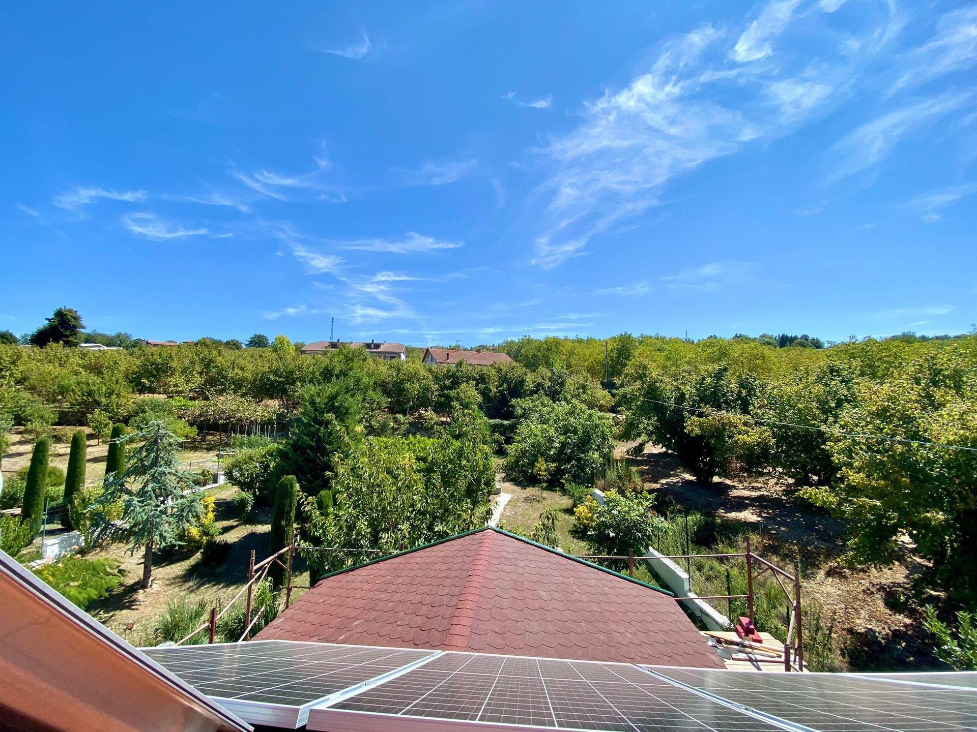 Weitläufiger Blick über Obstgärten und grüne Landschaft, mit Solarpaneelen auf dem Dach im Vordergrund.