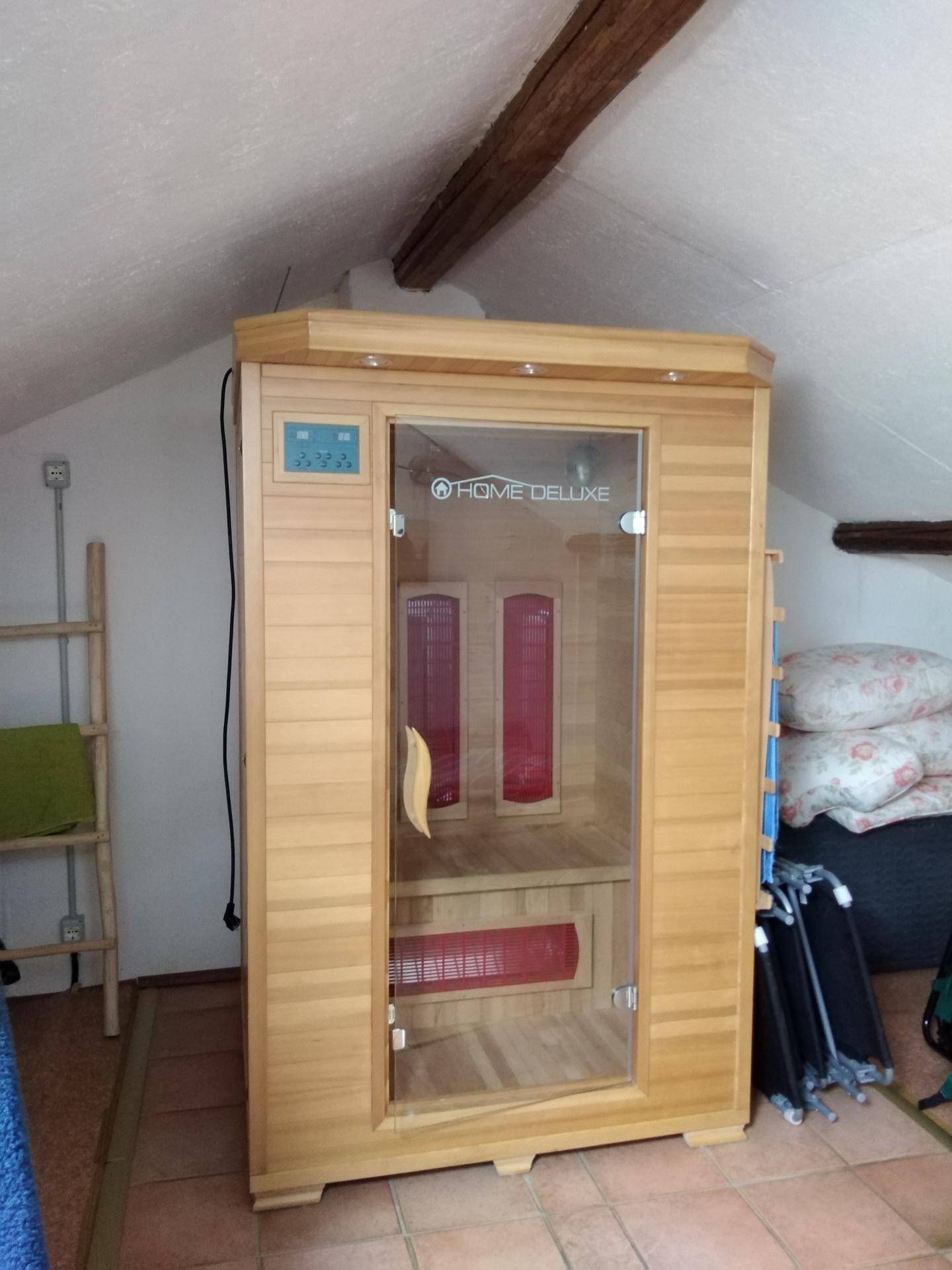 Infrarotsaunakabine in einem Dachzimmer mit sichtbarem Holzbalken und schräger Decke.