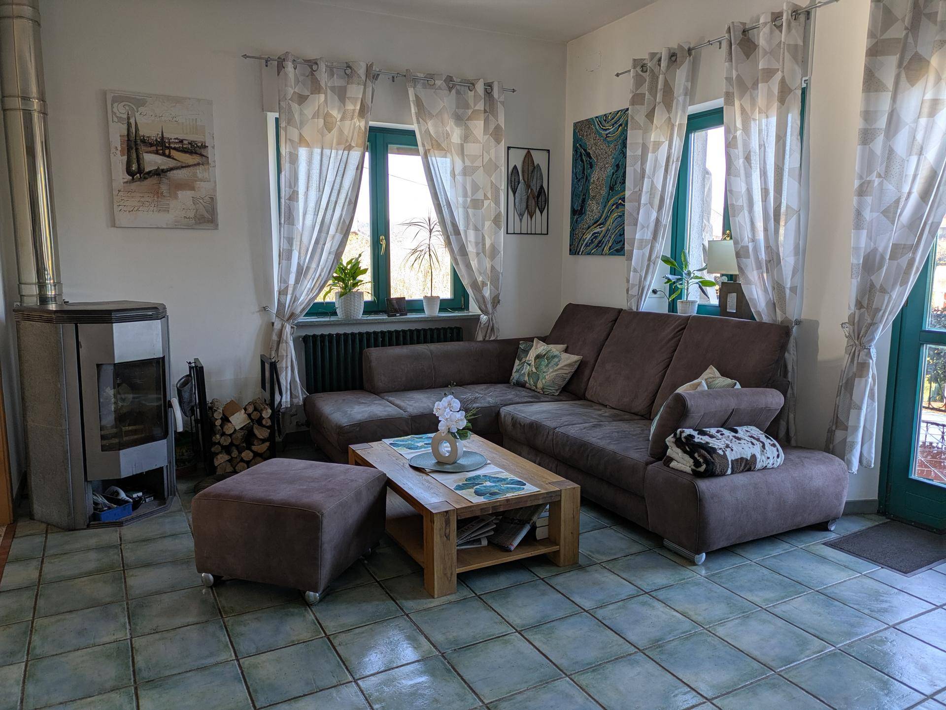 Helles Wohnzimmer mit bequemer Couch, Holzkamin und Fliesenboden, ideal zum Entspannen.