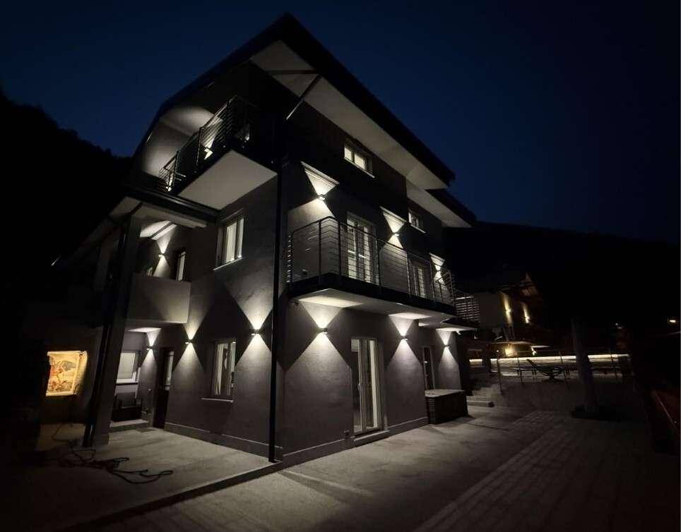 Die moderne Fassade des Gebäudes bei Nacht, stimmungsvoll beleuchtet von Wandleuchten.