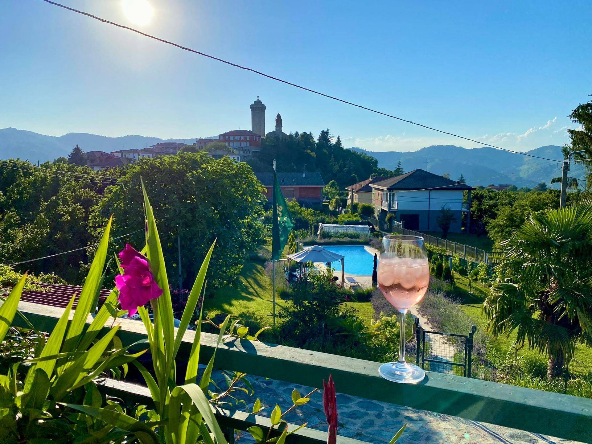 Panoramablick von einem Balkon auf die umliegende Landschaft, den Poolbereich und ein Dorf mit Turm.