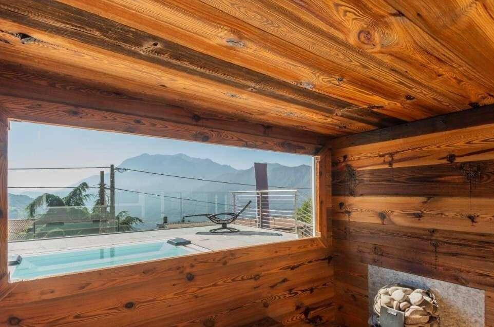 Gemütliche Sauna mit Holzverkleidung und großem Fenster mit Blick auf den Whirlpool und die Berge.