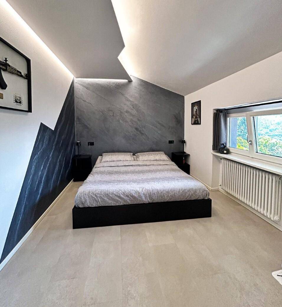 Modernes Schlafzimmer mit Dachschräge, Akzentwand und Blick auf die umliegende Landschaft.