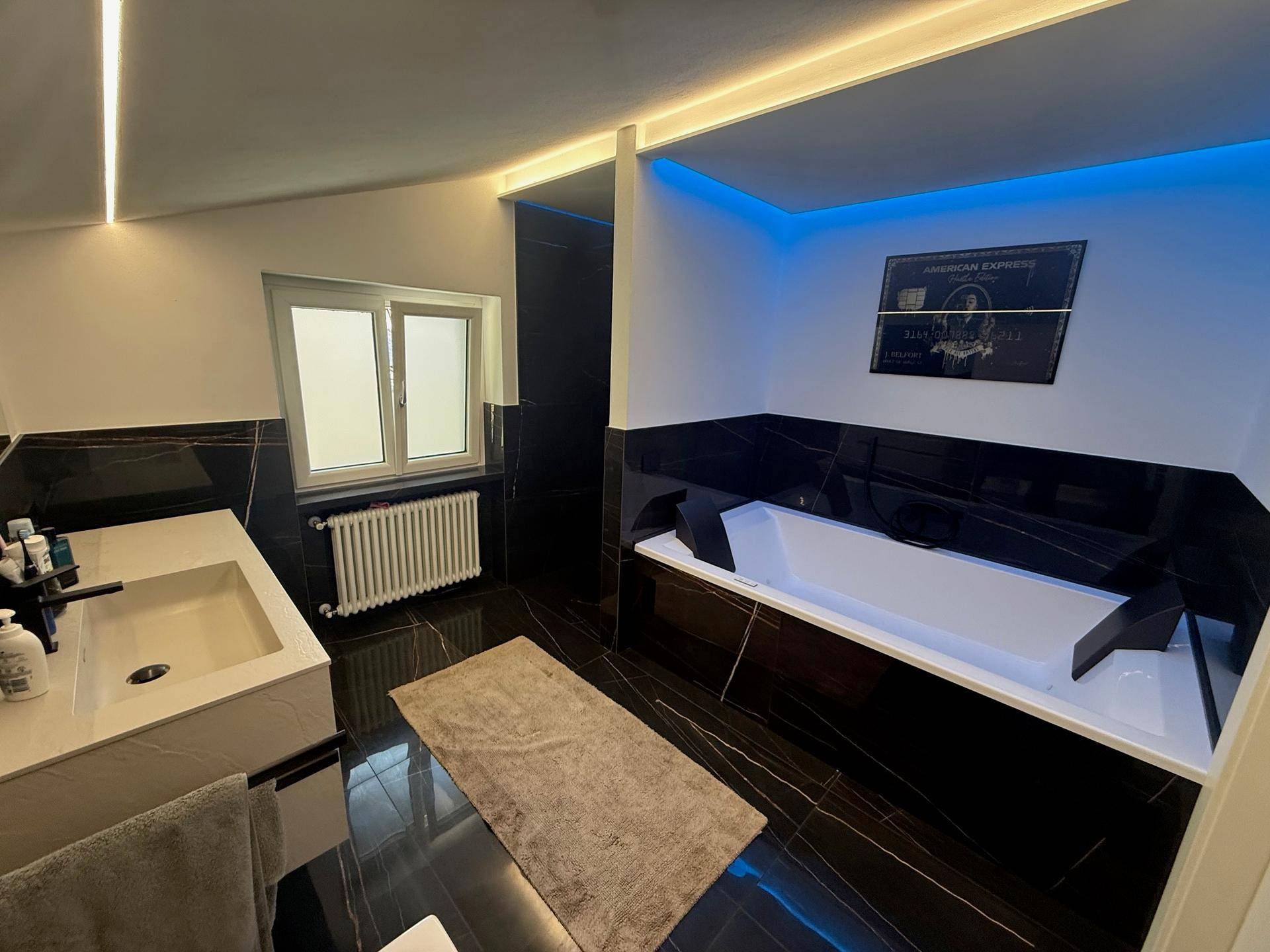 Luxuriöses Badezimmer mit schwarzen Marmorfliesen, moderner Badewanne und Fenster.