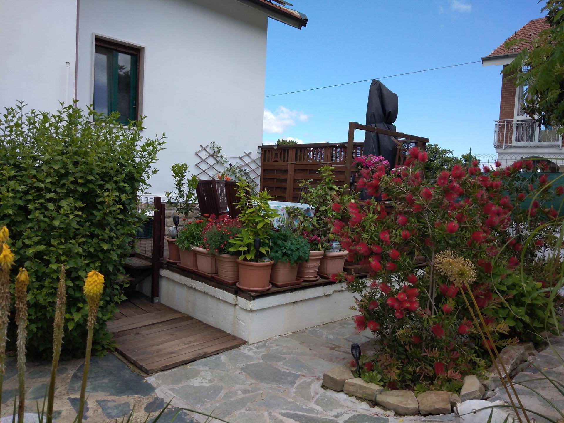 Gemütlicher gepflasterter Terrassenbereich neben dem Haus, geschmückt mit bunten Pflanzen und Blumen.