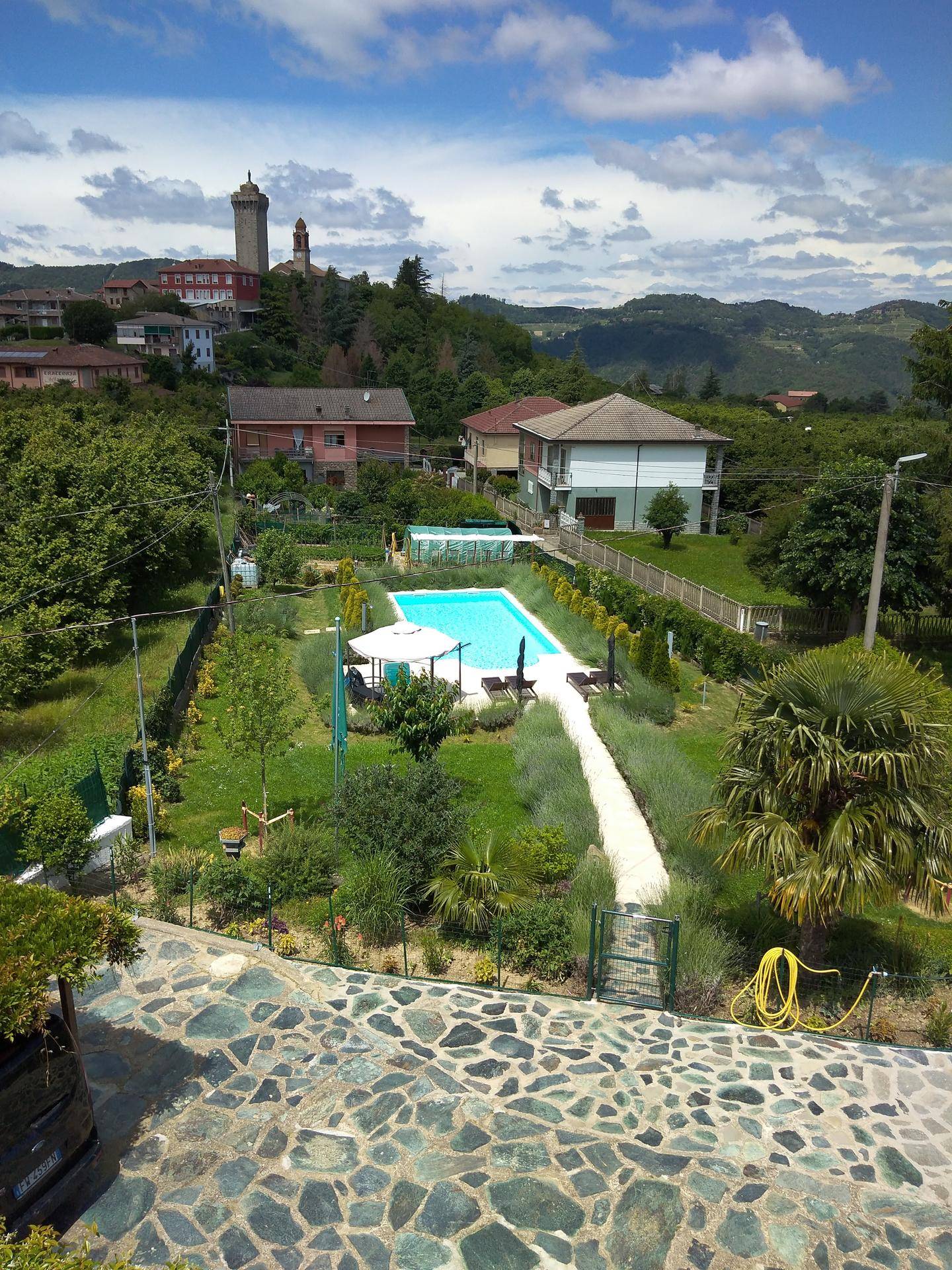 Vogelperspektive des weitläufigen Gartens mit Pool, umgeben von Häusern und grüner Hügellandschaft.