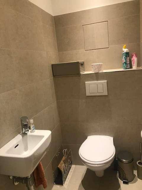Separates WC mit Wand-WC, kleinem Waschbecken und beigefarbenen Wandfliesen.