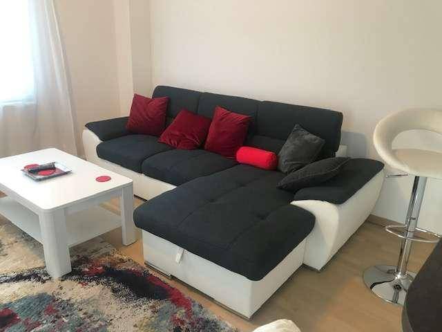 Gemütliches Wohnzimmer mit einem großen Ecksofa, farbigen Kissen und einem modernen Couchtisch.