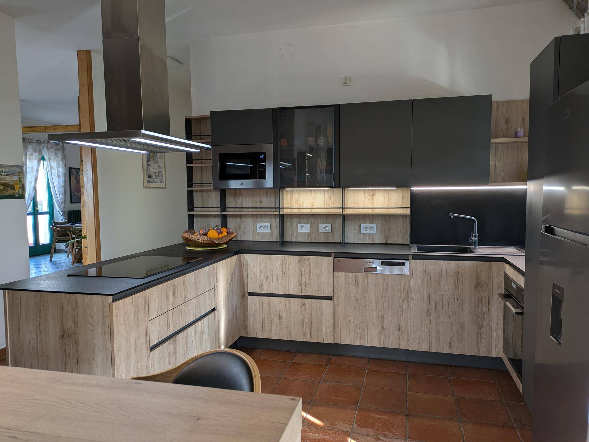 Moderne Küche mit dunklen und hellen Holzfronten, integrierten Geräten und Terrakottafliesenboden.