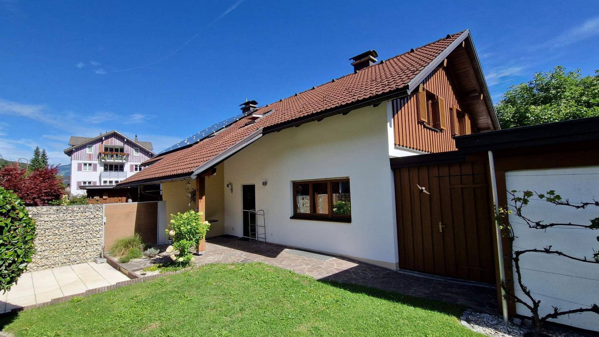 Seitenansicht des Hauses mit Ziegeldach, Garten und einem weiten Blick auf die Berge.