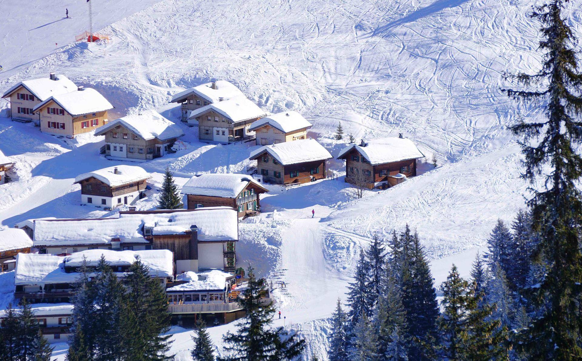 Malerisches Bergdorf mit verschneiten Chalets und Skipisten in den Alpen.