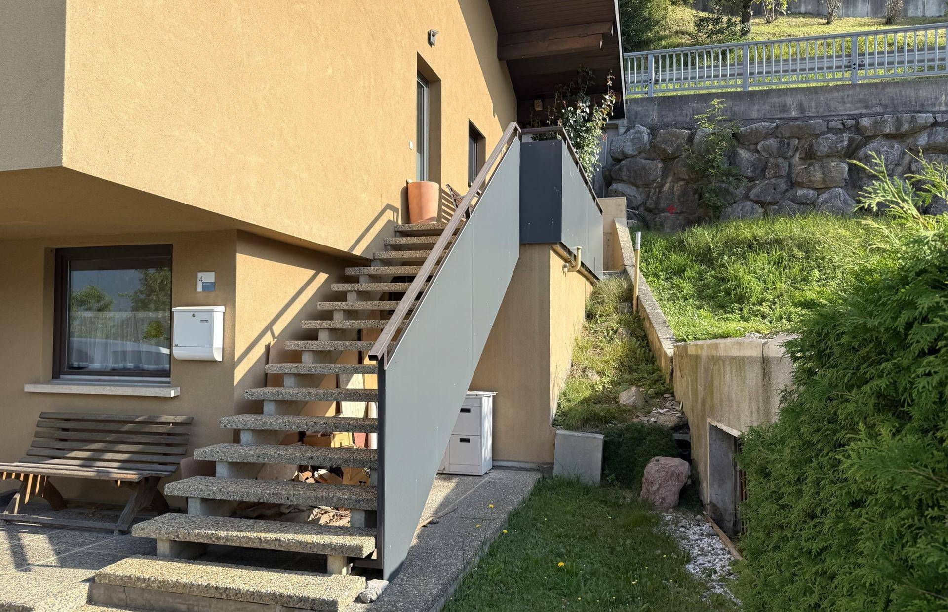 Außentreppe führt zum Eingang des Hauses, umgeben von Grün und Hanglage.