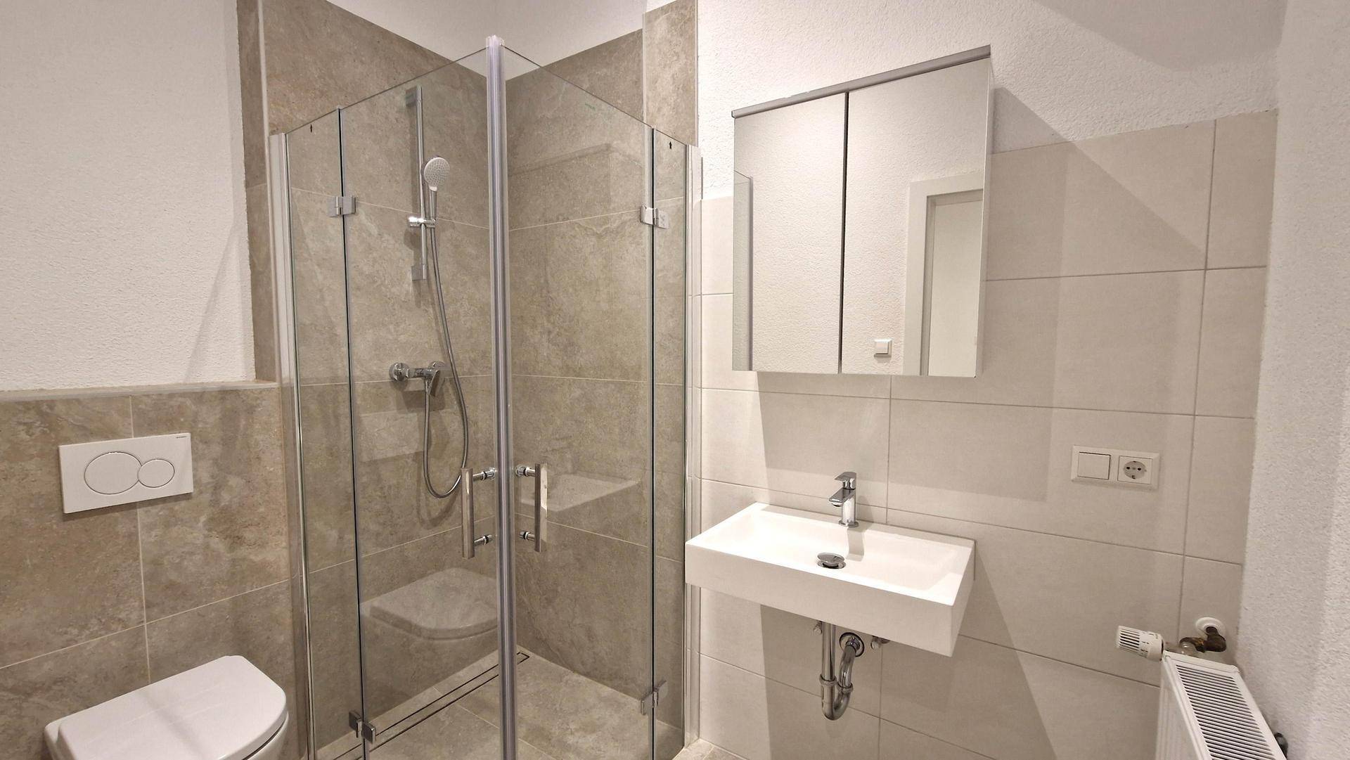 Modernes Badezimmer mit begehbarer Dusche, Wand-WC und hellem Fliesenboden in neutralen Farbtönen.