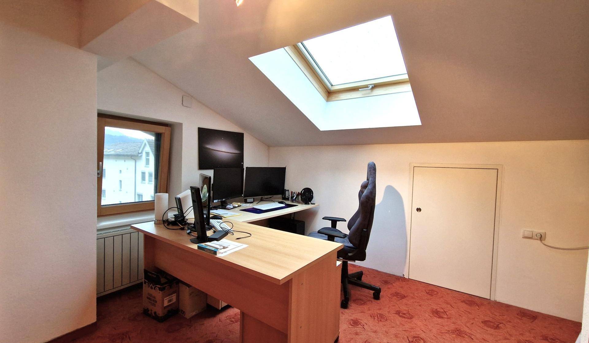 Dachgeschoss-Büro mit Schreibtisch, Computern und Dachfenster für viel Tageslicht.