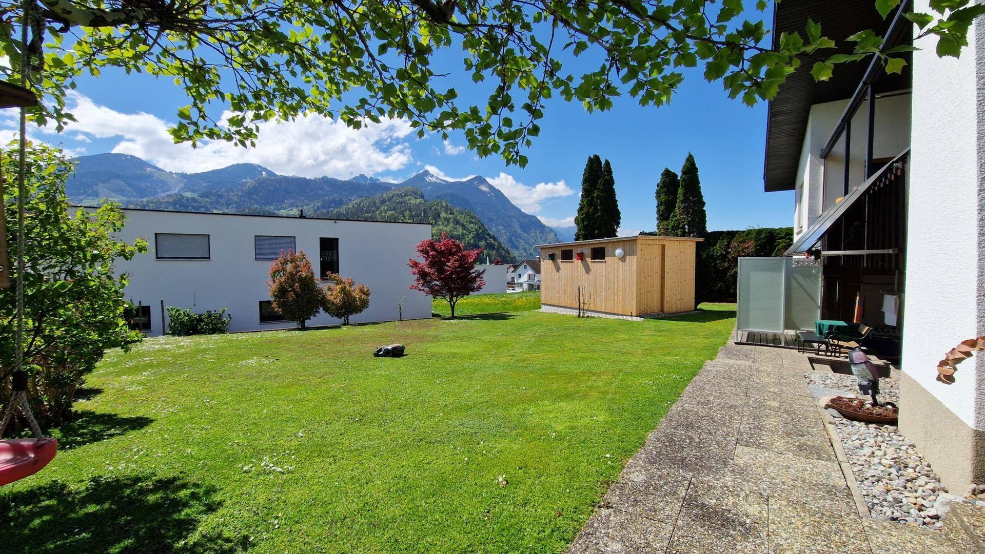 Weitläufiger Garten mit Rasenfläche, Gartenhaus und Blick auf die umliegende Berglandschaft.