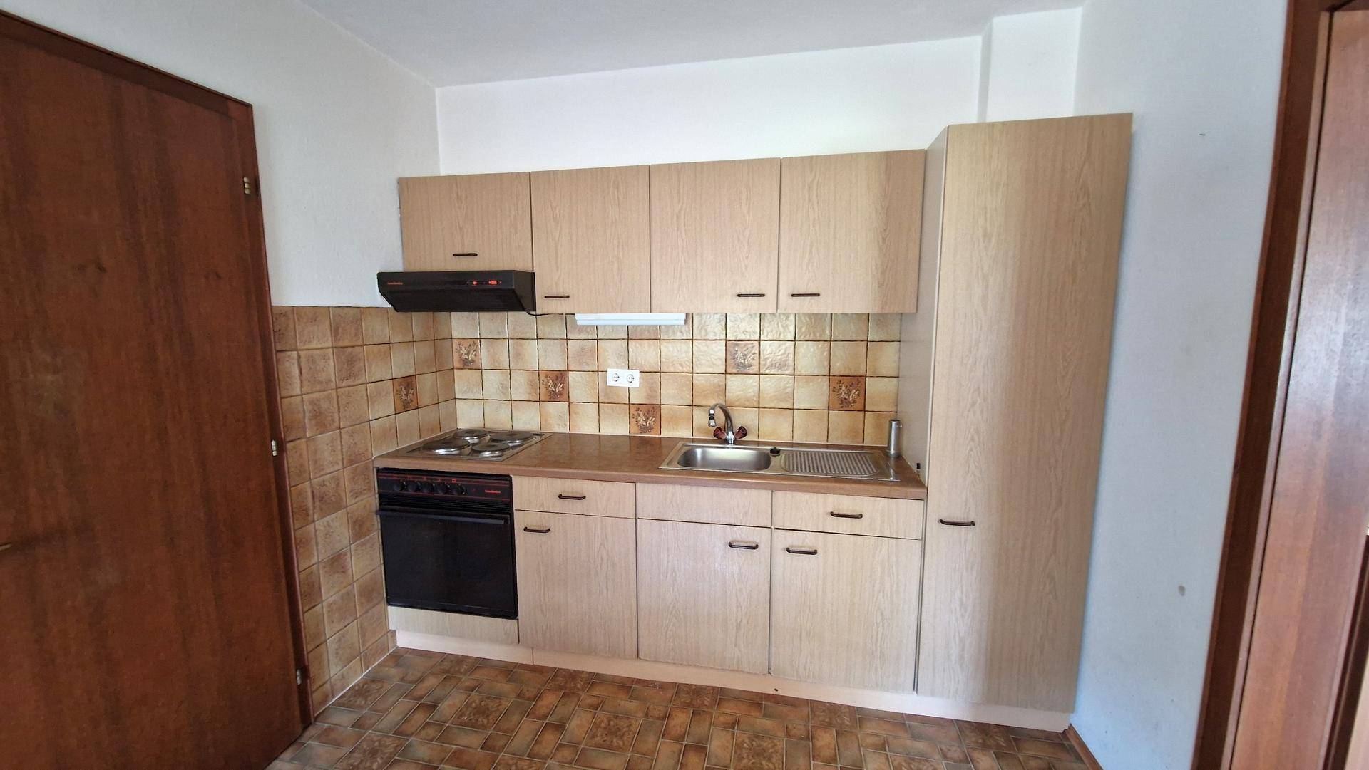 Kleine Küche mit hellen Holzschränken, Fliesenrückwand und grundlegenden Kochgeräten.