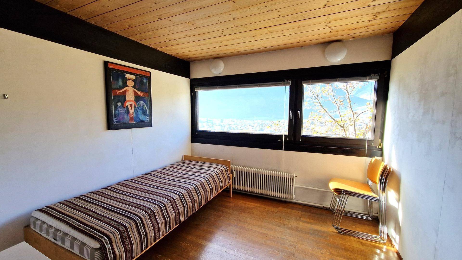 Gemütliches Schlafzimmer mit Einzelbett, Holzboden und Fenster mit Blick ins Grüne.