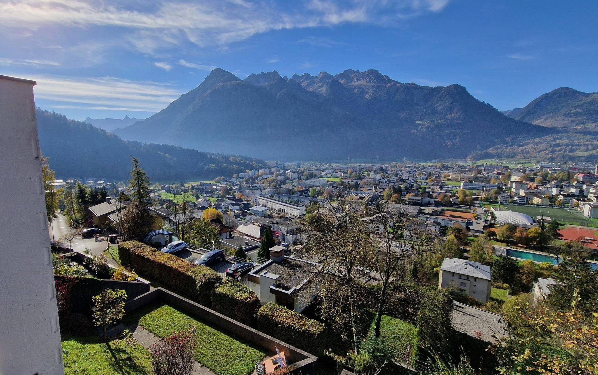 Panoramablick auf eine malerische Stadt und majestätische Berge unter strahlend blauem Himmel.