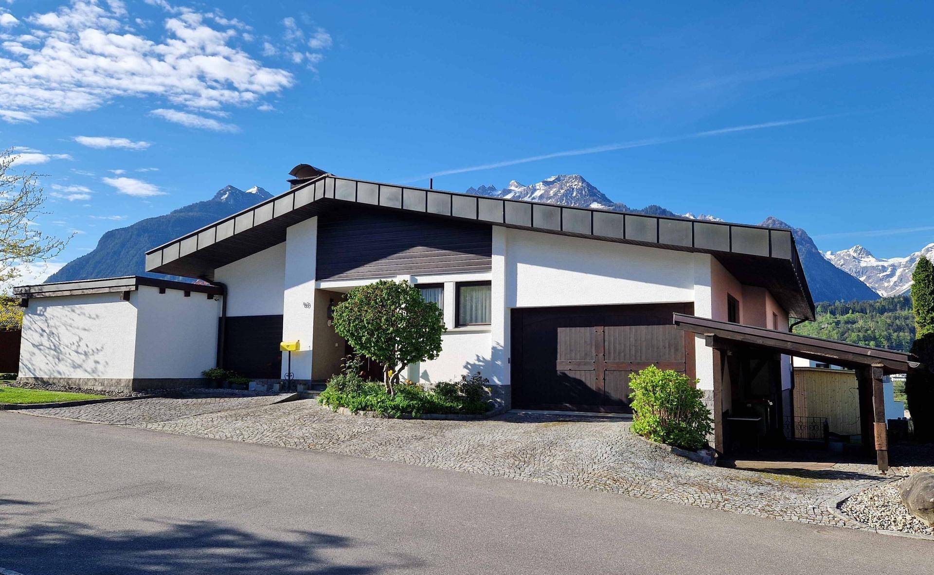 Ansicht des Hauses von der Straße mit Carport und beeindruckendem Bergpanorama.