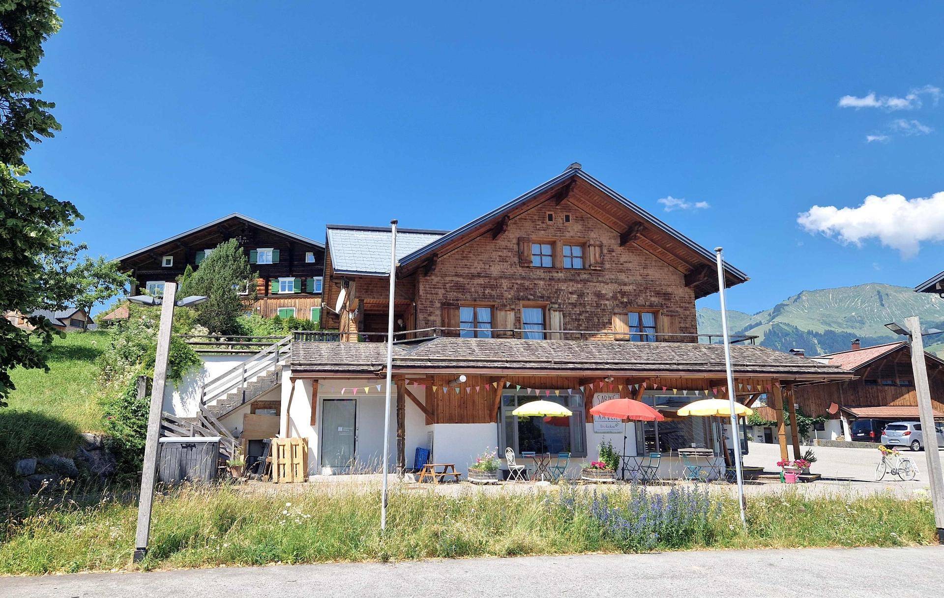 Traditionelles Holzhaus im Alpenstil mit Geschäften im Erdgeschoss und Bergblick.