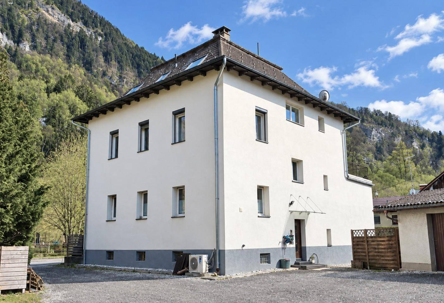 Rückansicht des Hauses mit weißer Fassade, Satteldach und Bergblick im Hintergrund.
