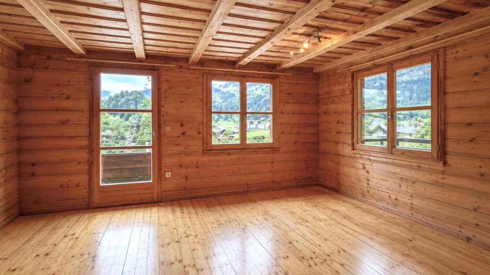 Heller Raum mit Holzboden, Holzvertäfelung und Zugang zu einem kleinen Balkon mit Bergblick.