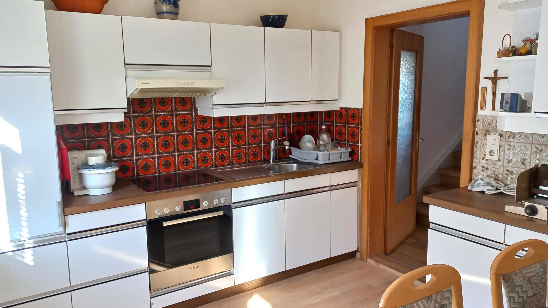 Helle Küche mit weißen Schränken, roten Fliesen als Spritzschutz und modernen Geräten.