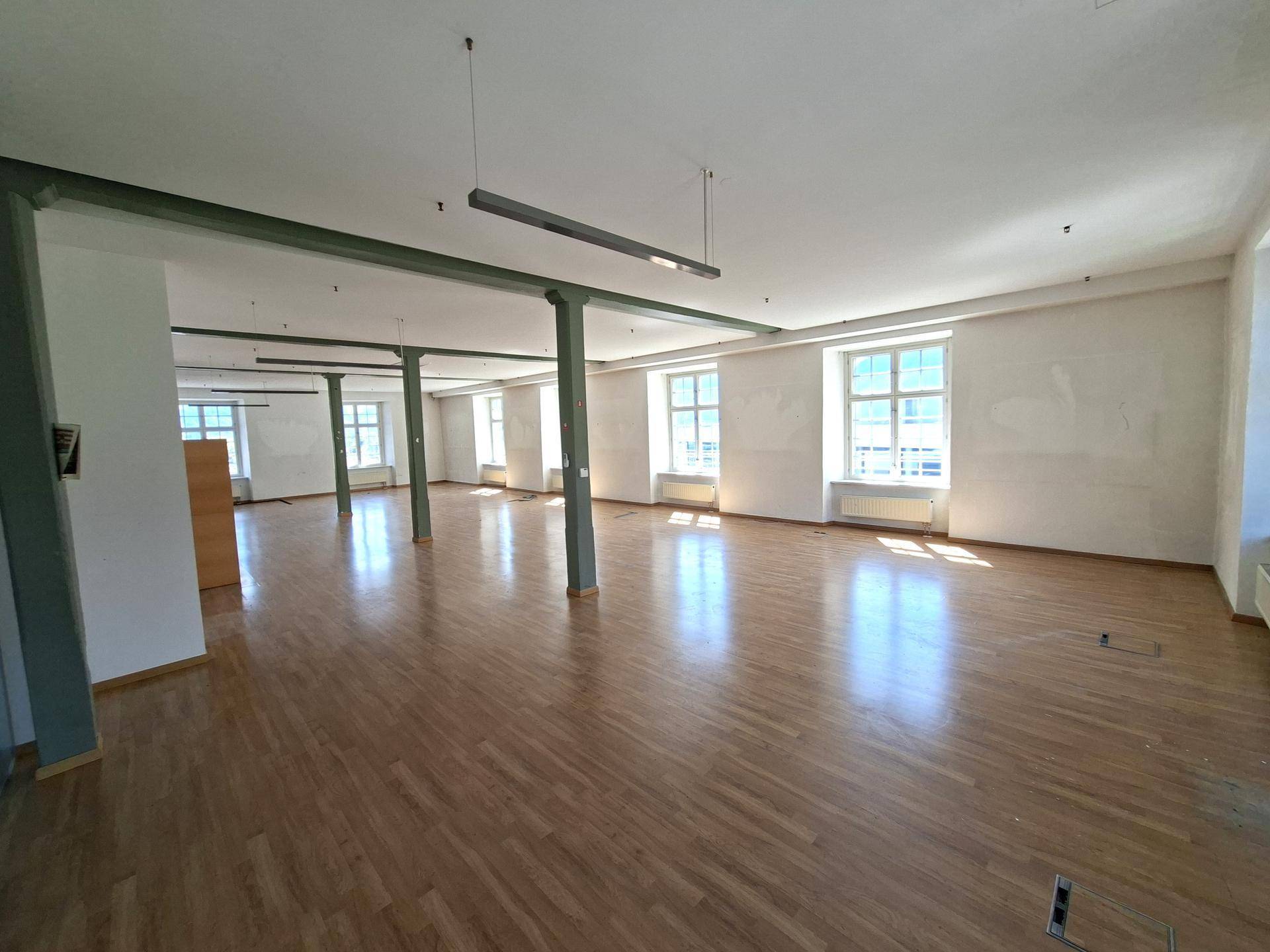 Großer, offener Bürobereich mit Holzboden, hohen Decken und modernen Hängelampen.