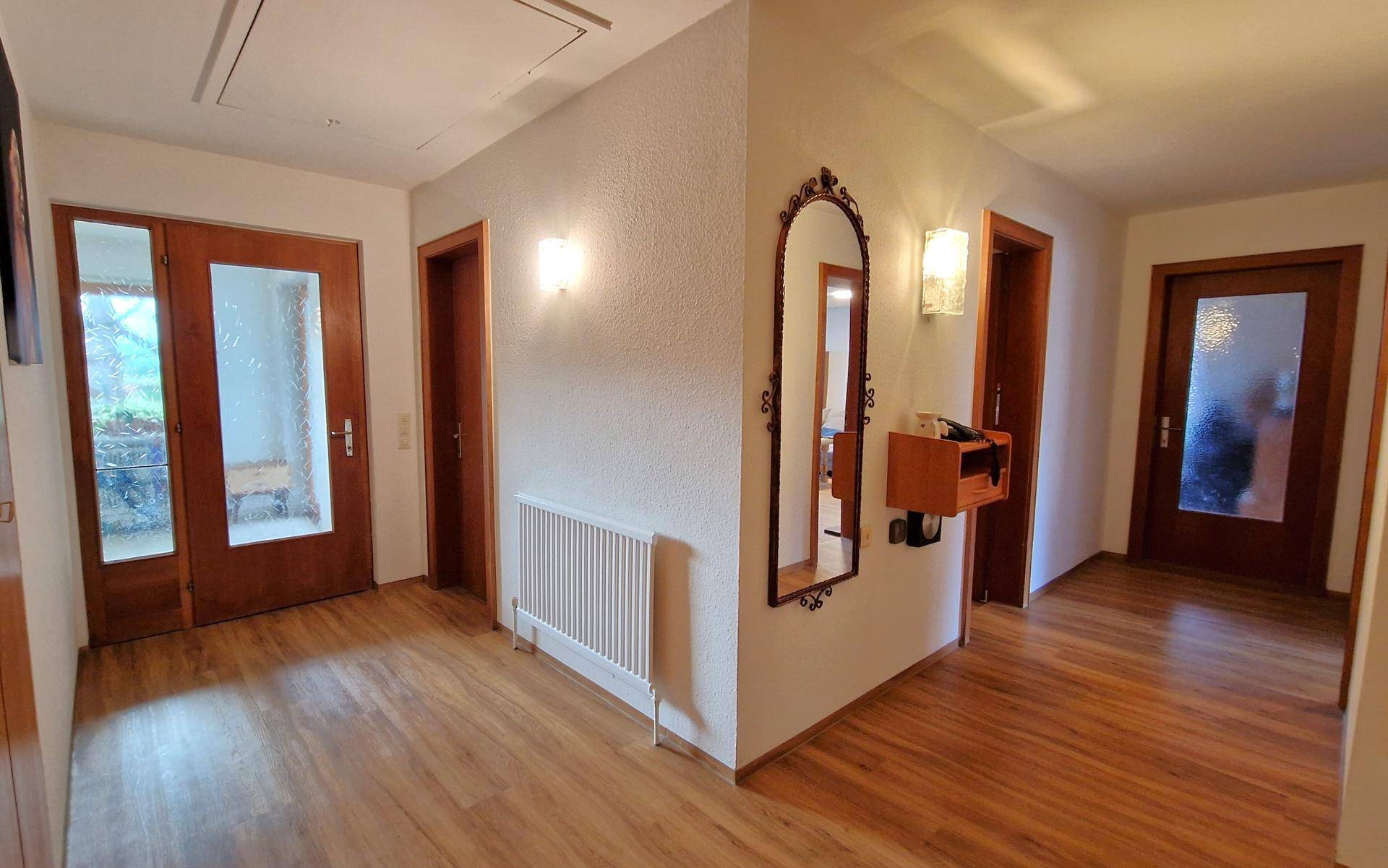 Geräumiger Flur mit Holzfußboden, dekorativem Spiegel und mehreren Zugangstüren.