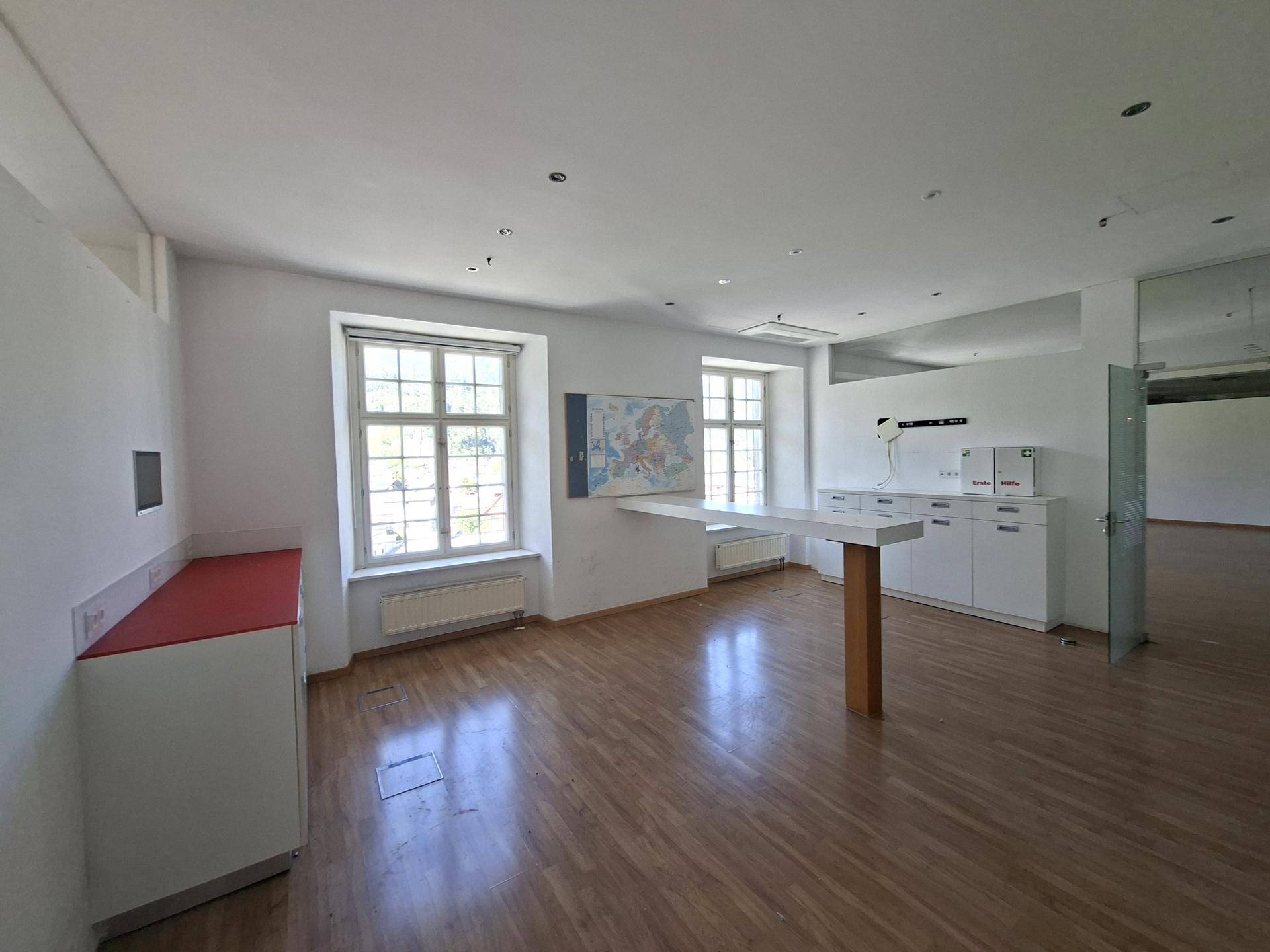 Heller Büroraum mit Holzboden, großen Fenstern und integrierten Schränken und Arbeitsflächen.