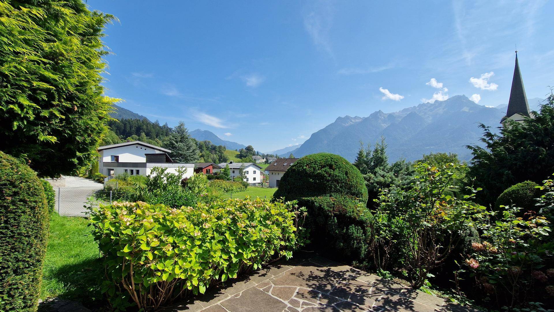 Gepflasterter Gartenbereich mit üppiger Bepflanzung und weitem Blick auf die Berge.