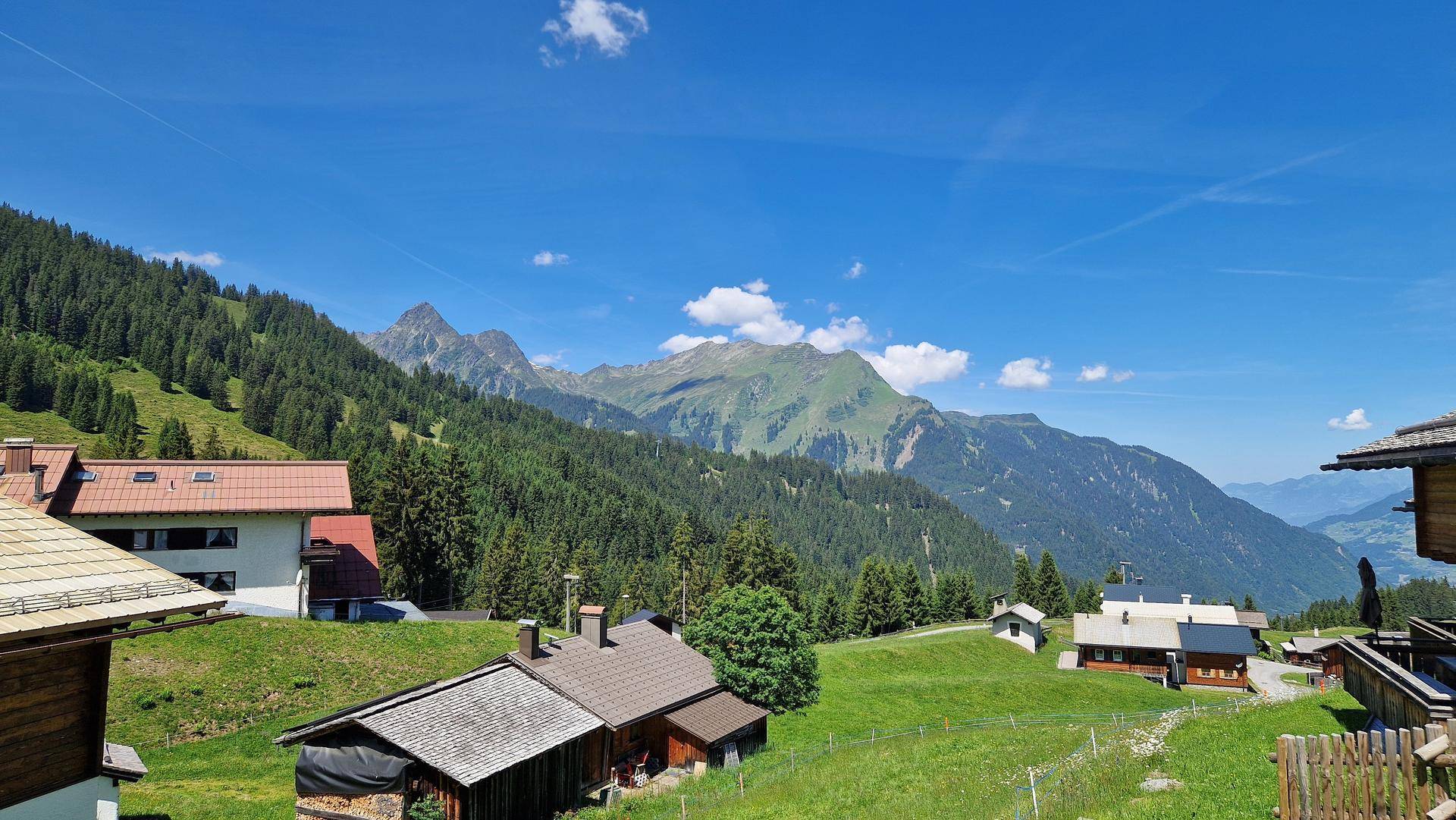Idyllische Alpenlandschaft mit verstreuten Häusern und üppigen grünen Bergen im Sommer.