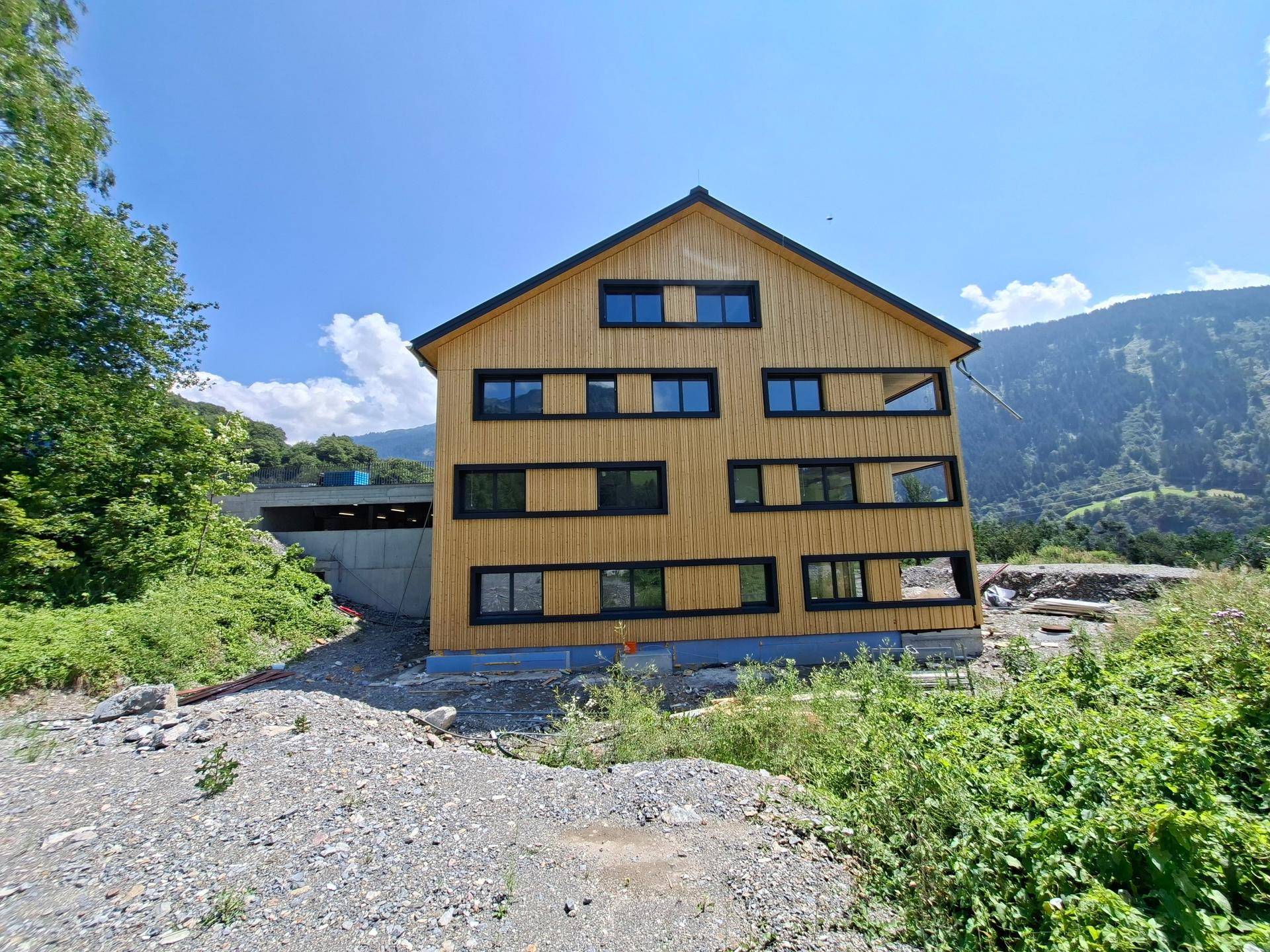 Rückansicht des Neubaus mit Holzverkleidung und Zufahrt zu einer Tiefgarage.