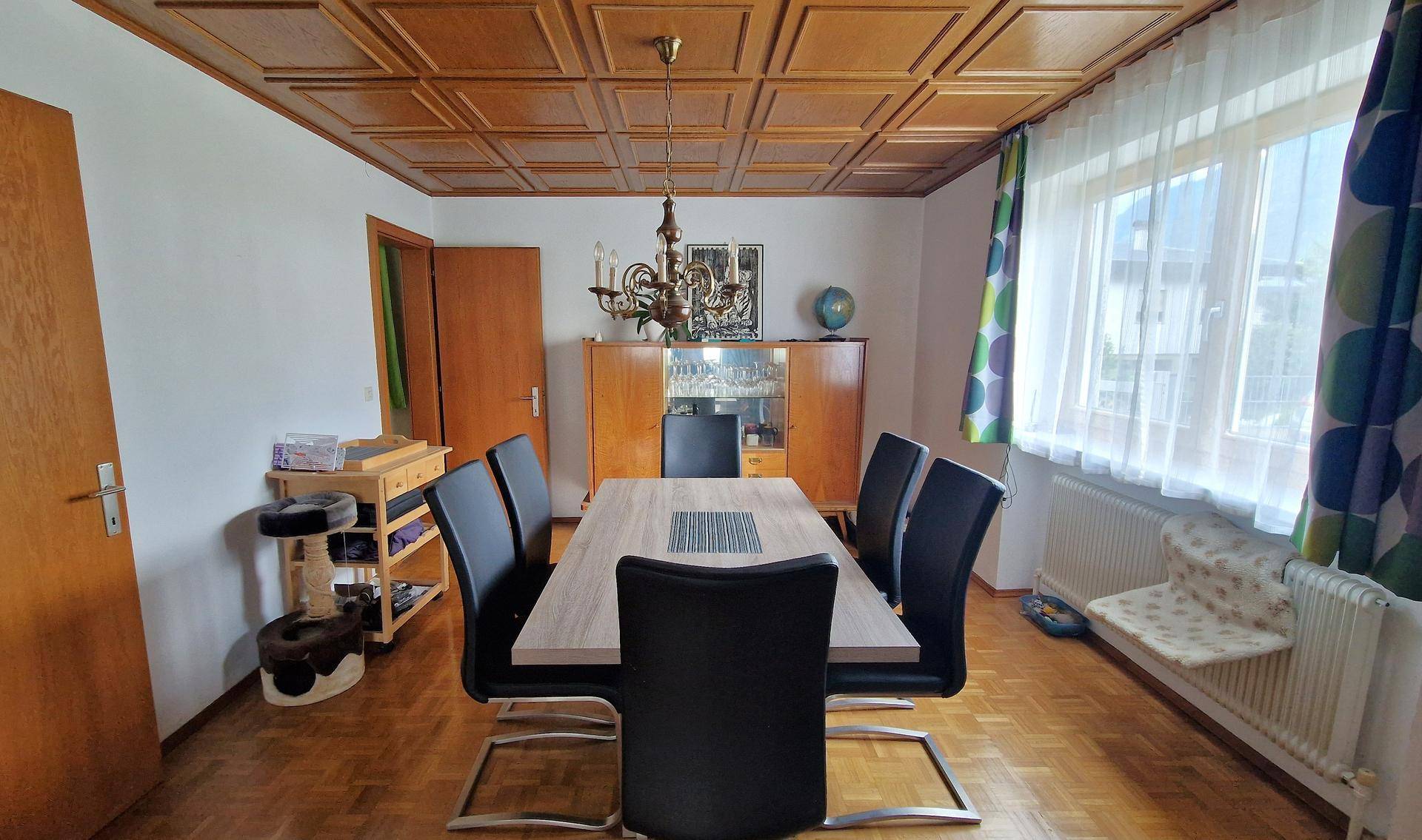 Esszimmer mit Holztäfeldecke, großem Esstisch und Blick nach draußen.