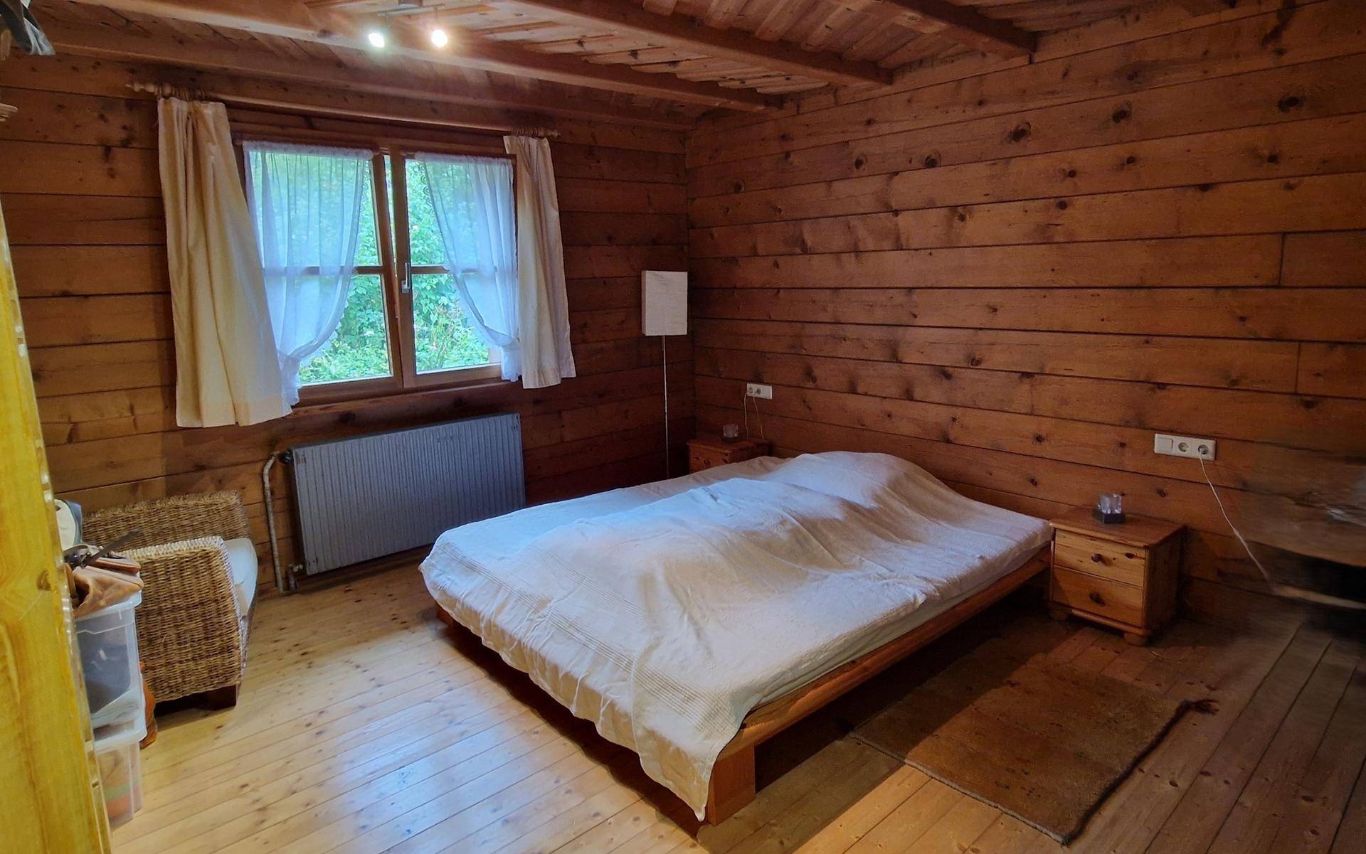 Schlafzimmer mit Holzboden, Holzvertäfelung, Doppelbett und Fenster mit Blick ins Grüne.
