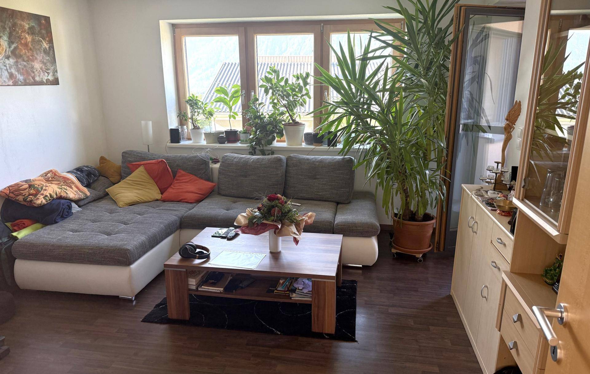 Geräumiges Wohnzimmer mit großem Ecksofa, vielen Pflanzen und Zugang zum Balkon.