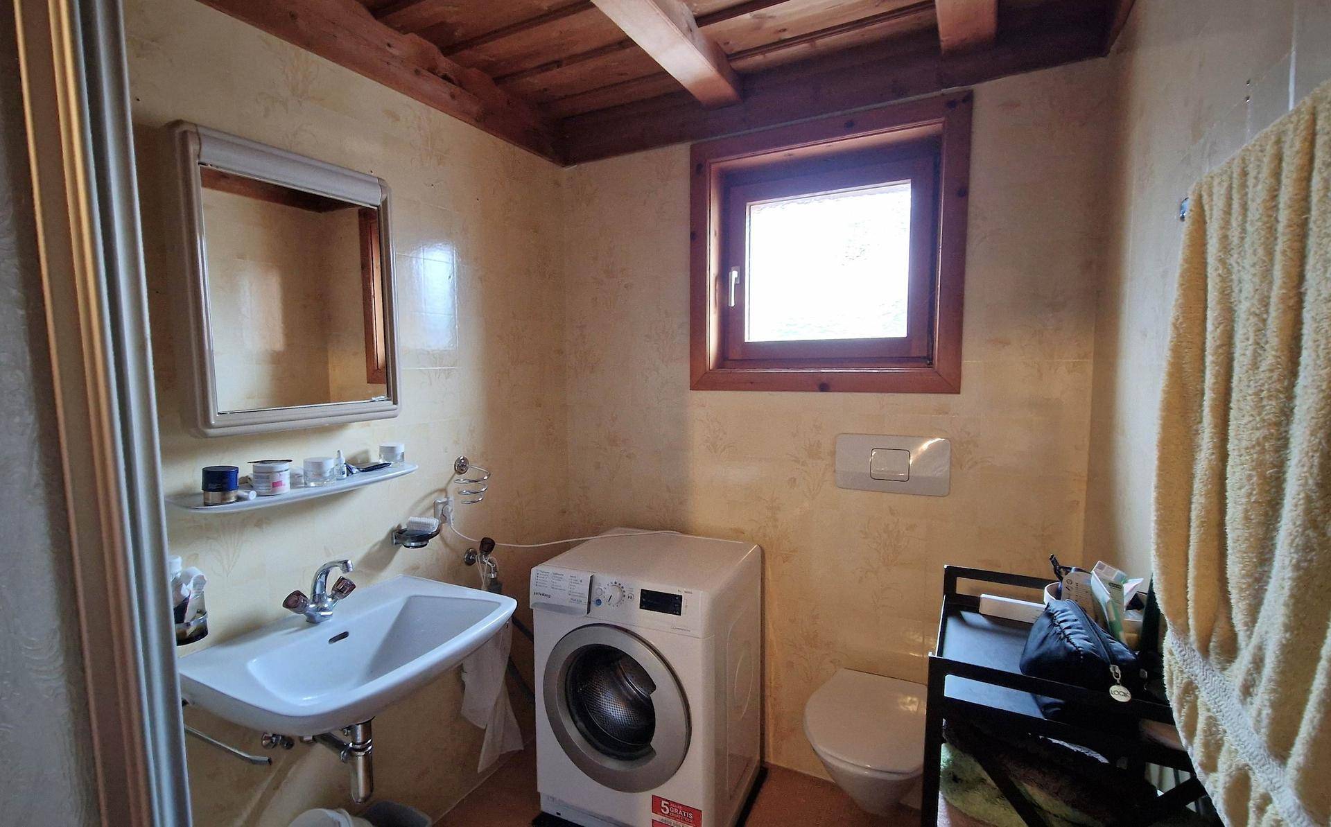Helles Badezimmer mit Waschbecken, Toilette, Waschmaschine und Fenster.