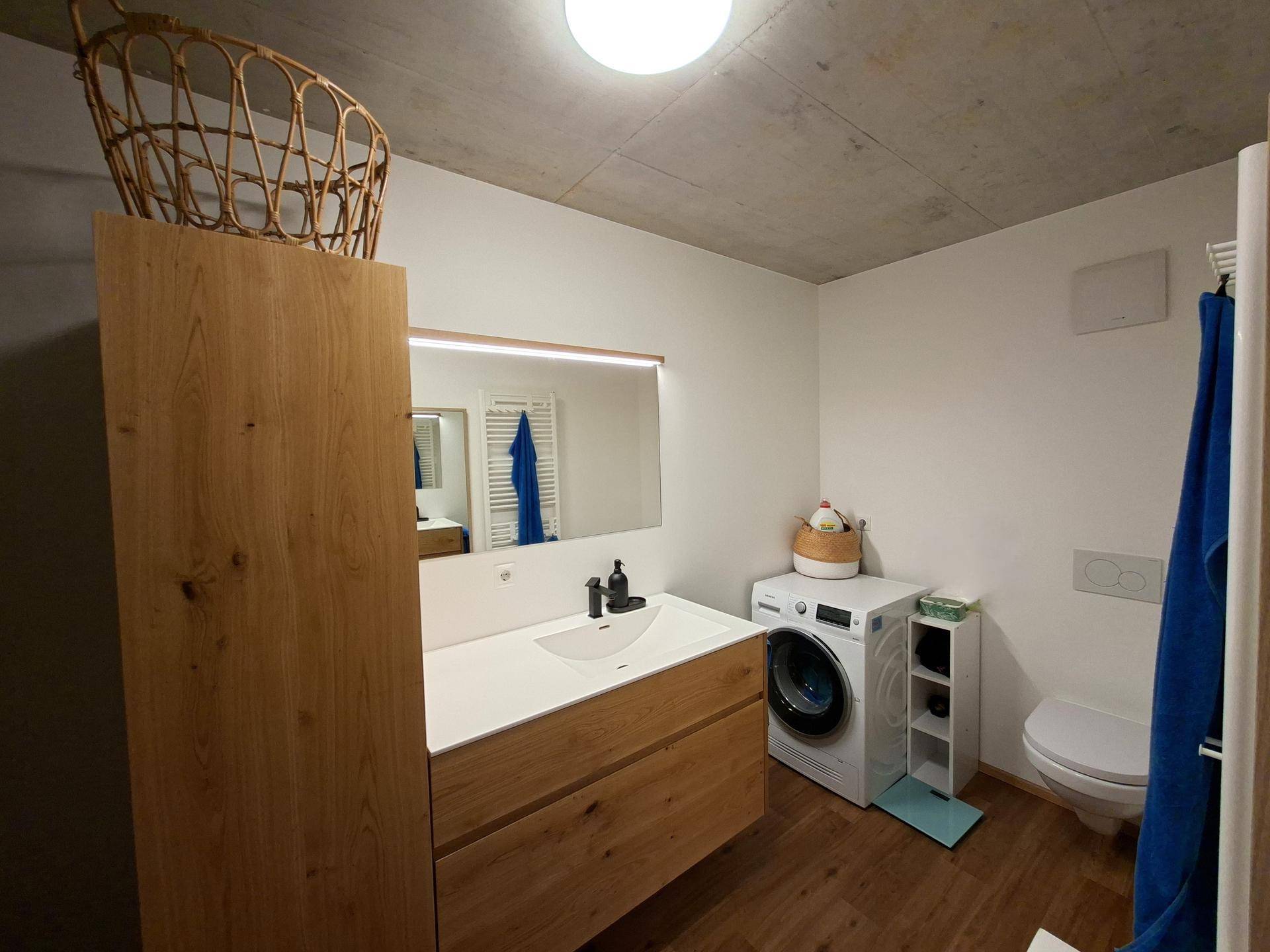 Helles Badezimmer mit modernem Holzwaschtisch, Spiegel und integrierter Waschmaschine.