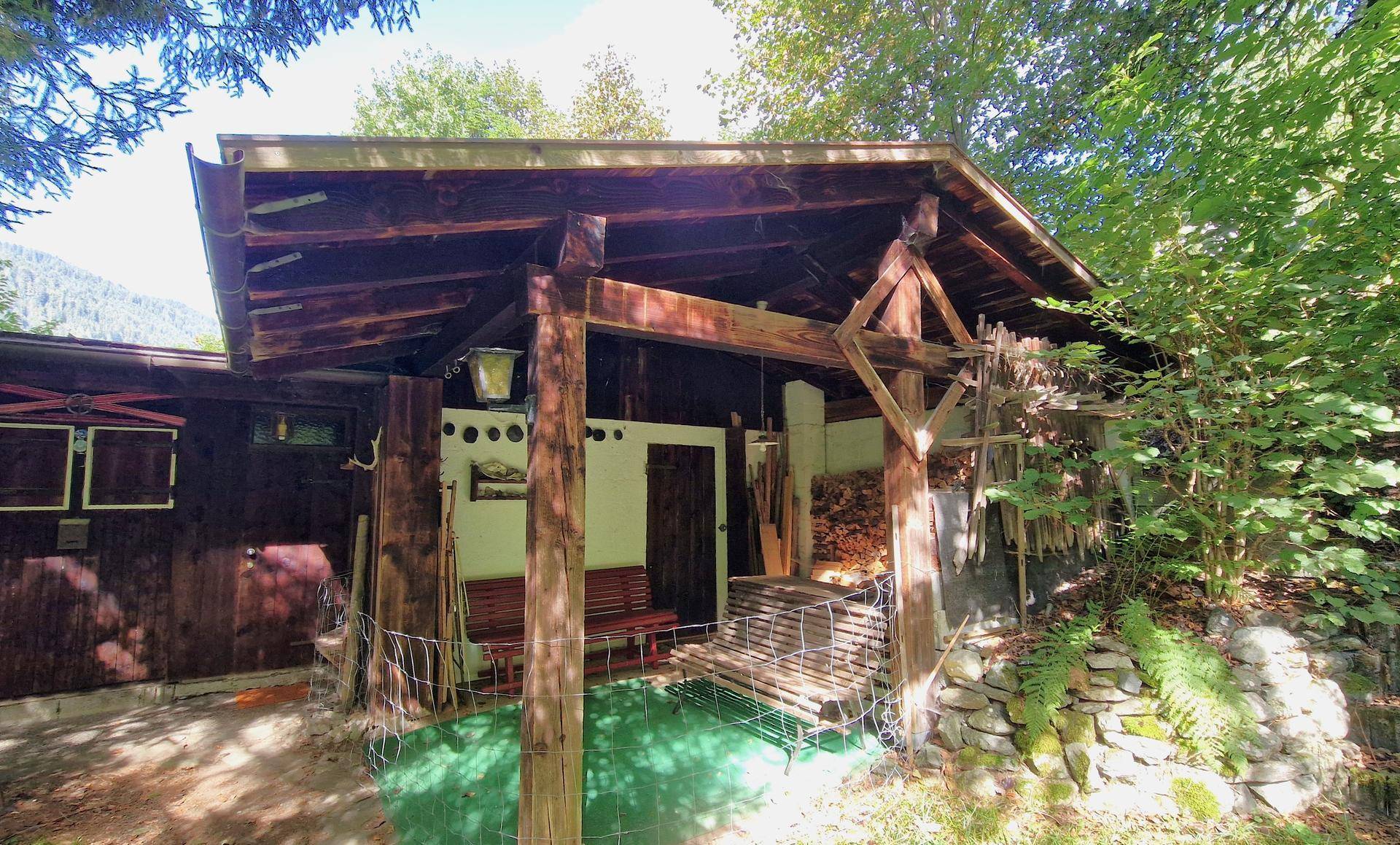 Überdachter Außenbereich eines Holzhauses mit sichtbaren Holzbalken und einem Stapel Brennholz.