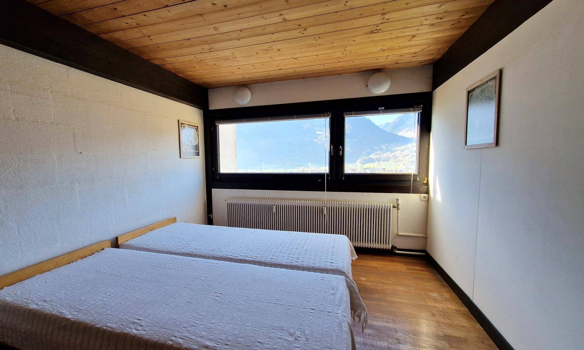 Helles Schlafzimmer mit zwei Betten, Holzboden und Fenster mit Panoramablick.